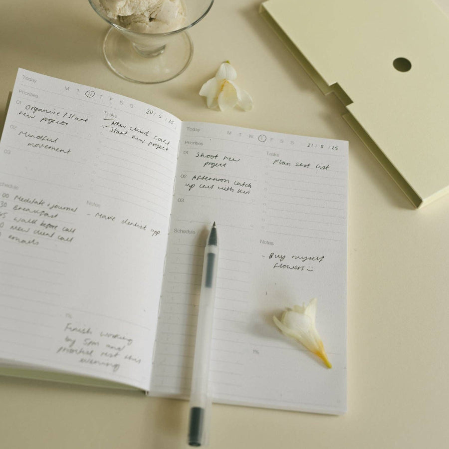 Open notebook with handwritten notes, a pen, ice cream, and flowers on a light surface