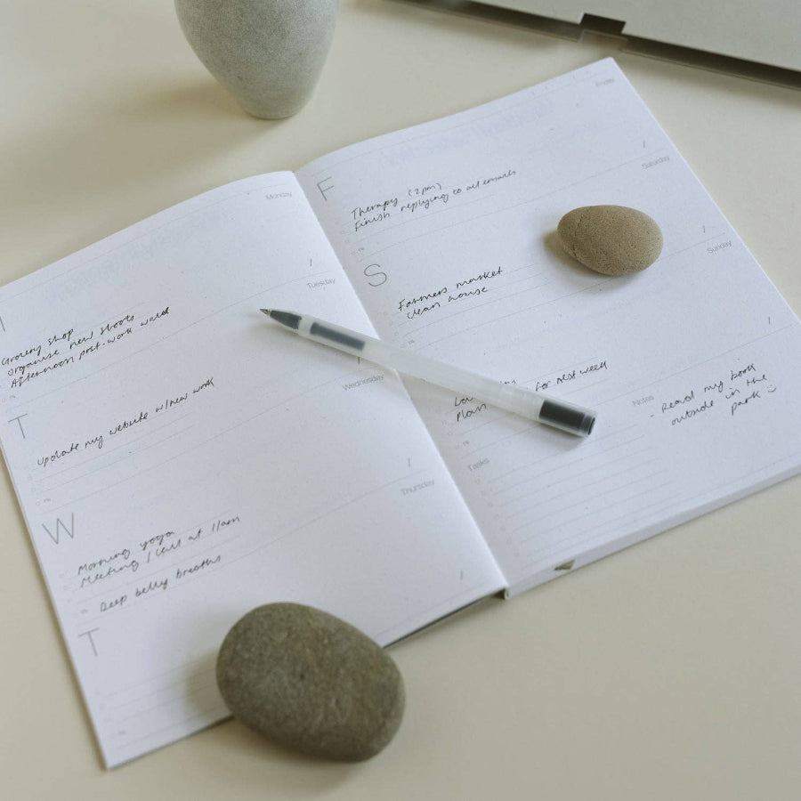 Open notebook with writing, pen, and stones on a light surface