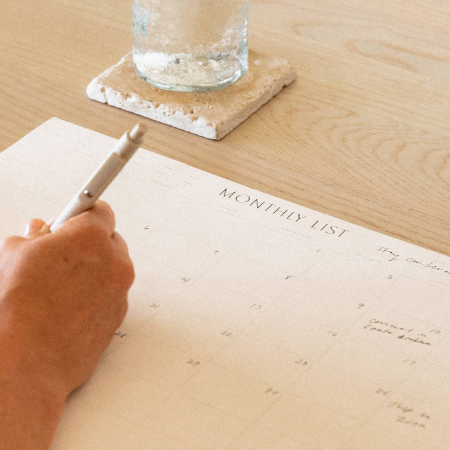 Hand writing in a planner with a glass of water on a wooden table