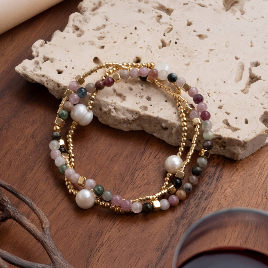 Stack of beaded bracelets on a wooden surface with a stone and branch in the background