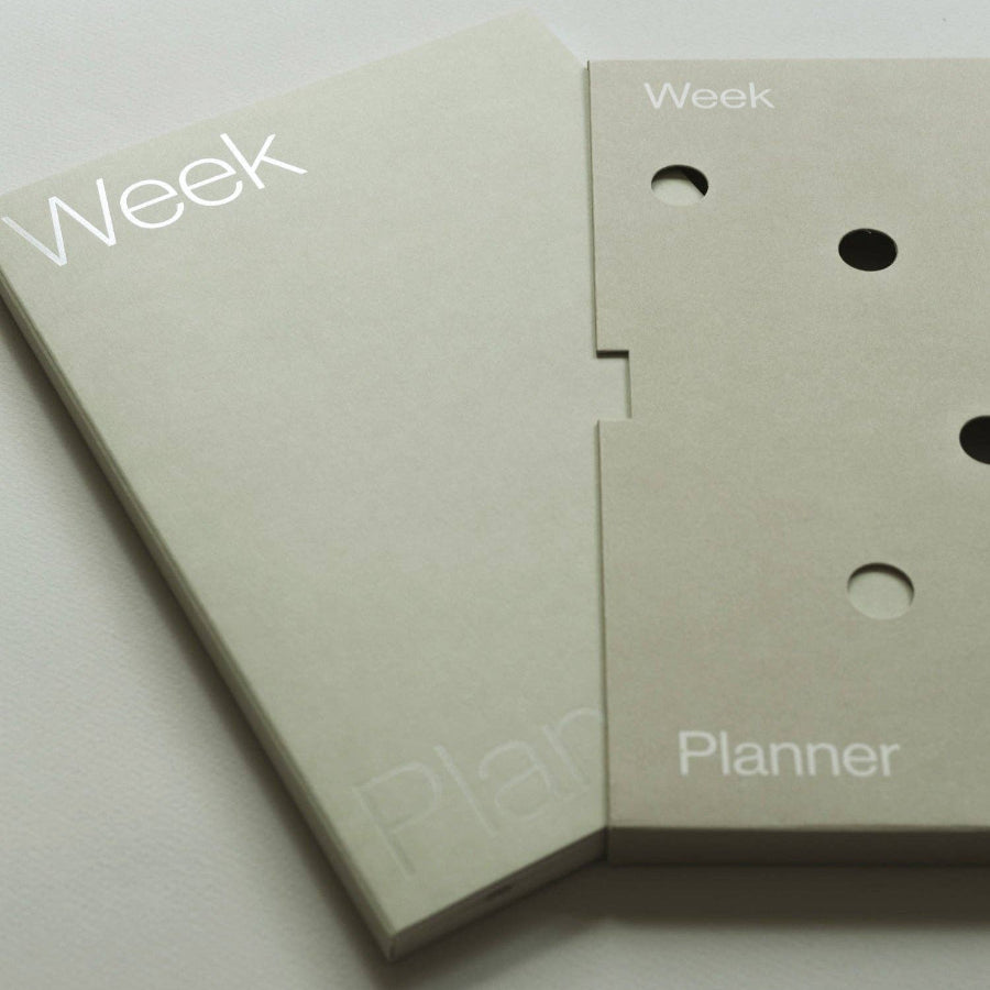 Close-up of a beige planner with 'Week' and 'Planner' text on a light gray background