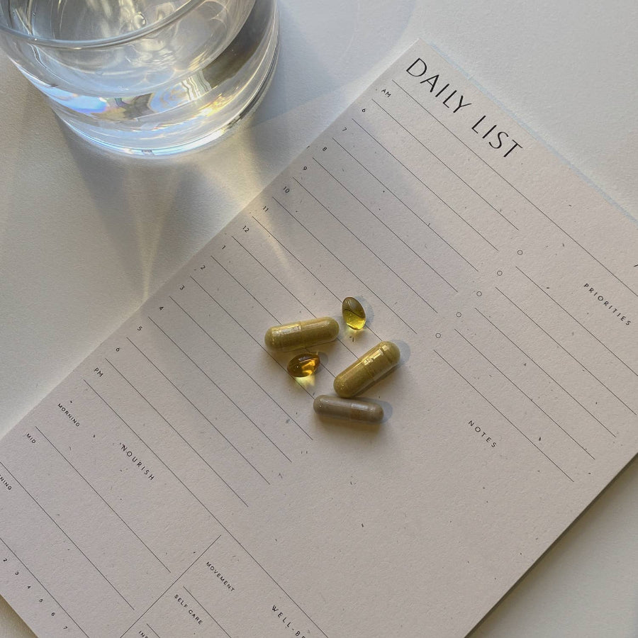 Gold capsules on a daily planner with a glass of water